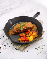 Steak with gravy and vegetables in a cast iron skillet on a white marble surface.
