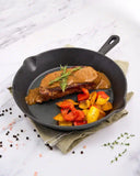 Steak with gravy and vegetables in a cast iron skillet on a white marble surface.