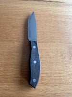 A Jumbo Wood Steak Knife with a serrated stainless steel blade and a round wooden handle with three rivets, displayed on a wooden surface.
