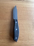 A Jumbo Wood Steak Knife with a serrated stainless steel blade and a round wooden handle with three rivets, displayed on a wooden surface.