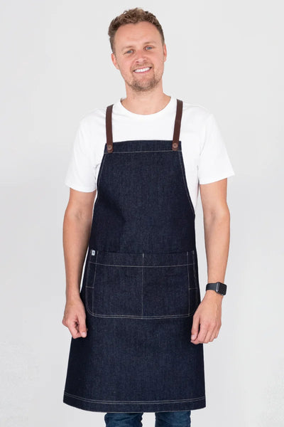 A person wearing a dark blue denim bib apron with brown straps and a white t-shirt.