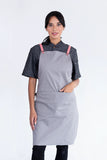 A person wearing a light gray bib apron with lemon herringbone straps and a black shirt underneath.