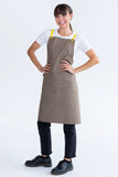 A person wearing a latte brown bib apron with lemon yellow straps and a white t-shirt underneath.