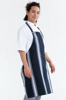 A person wearing a navy and white striped chef bib apron with adjustable neck loop over a white chef jacket.