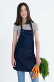 A child wearing a navy blue denim bib apron with a front pocket, neck loop, and waist ties, holding a bunch of carrots.