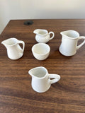 Five white ceramic pitchers on a wooden surface