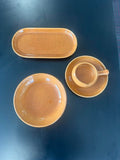 Set of ceramic dishes including a bowl, plate, platter and sauce dish with handle  on a dark surface