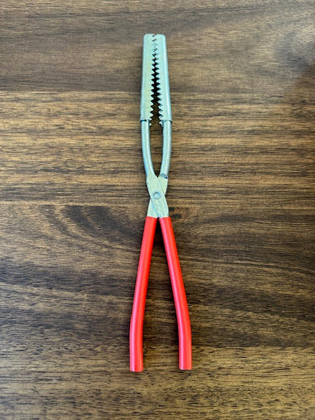 Fish gripper clamp Red Handle with Steel serrated Head on a wooden surface