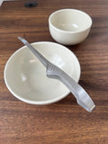 Two white bowls with a stainless steel serving tool