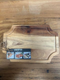 A rectangular wooden serving board with rounded corners and a dark stained top section, shown on a wood-grain surface. A small attached tag reads 'cerve' with small food photos.